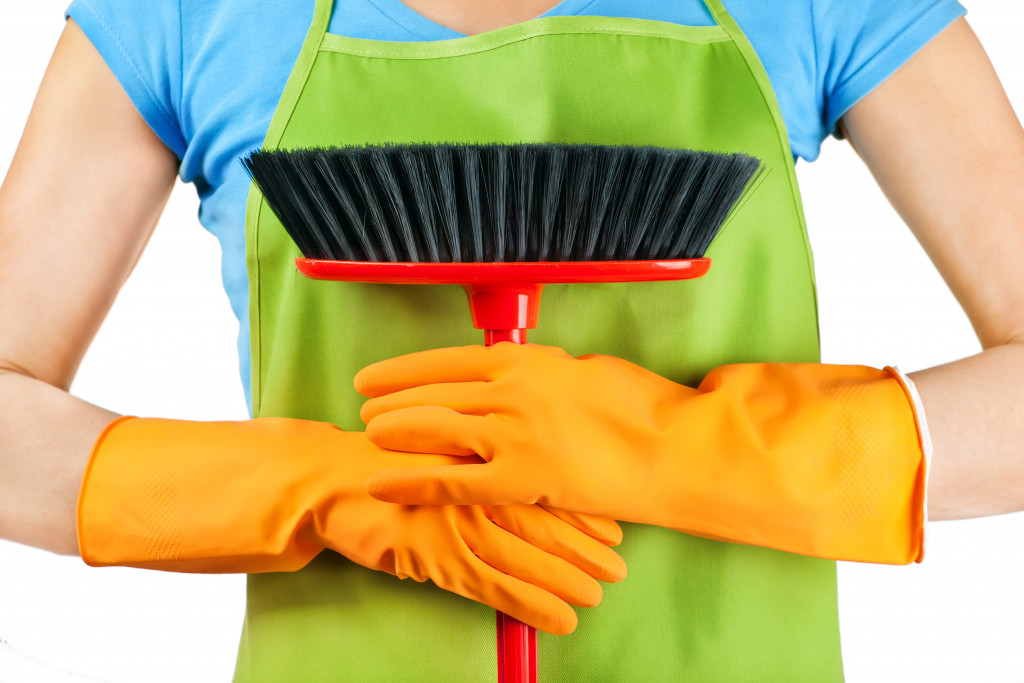 A person wearing an apron and gloves whole holding a broom
